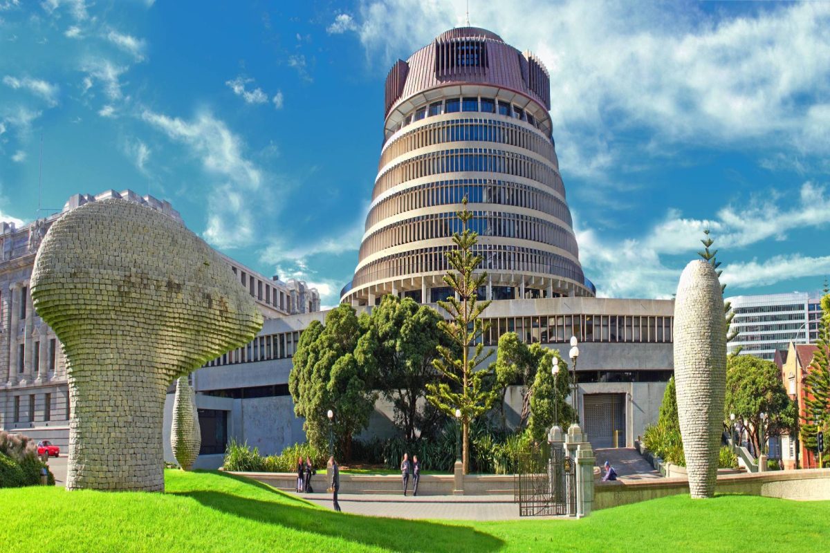 A round, modern government building with layered architecture, surrounded by sculptures, trees, and a grassy area