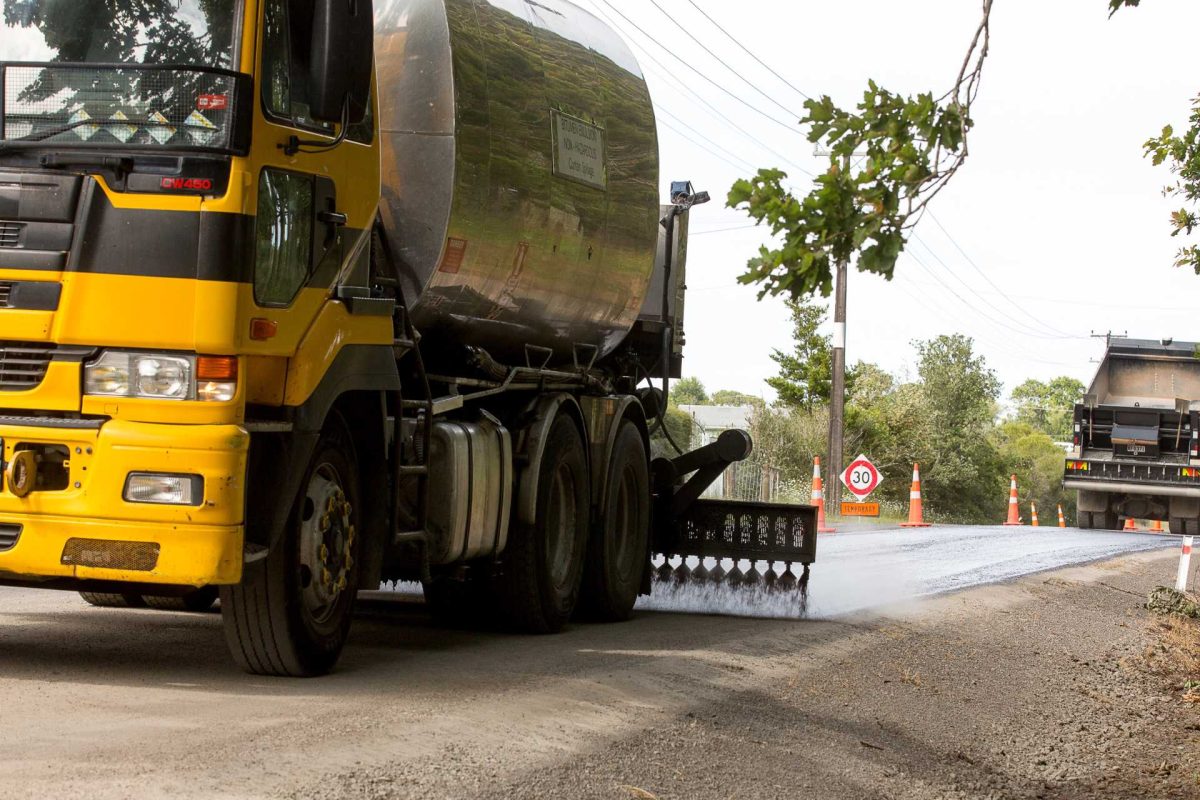 Yellow bitumen truck spraying surface during road sealing work