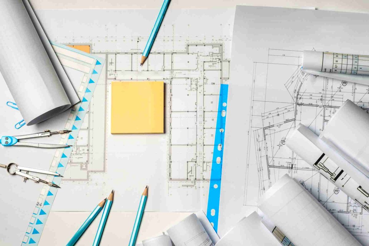 Architectural blueprints, rolled papers, compass, pencils, and sticky notes on a work surface