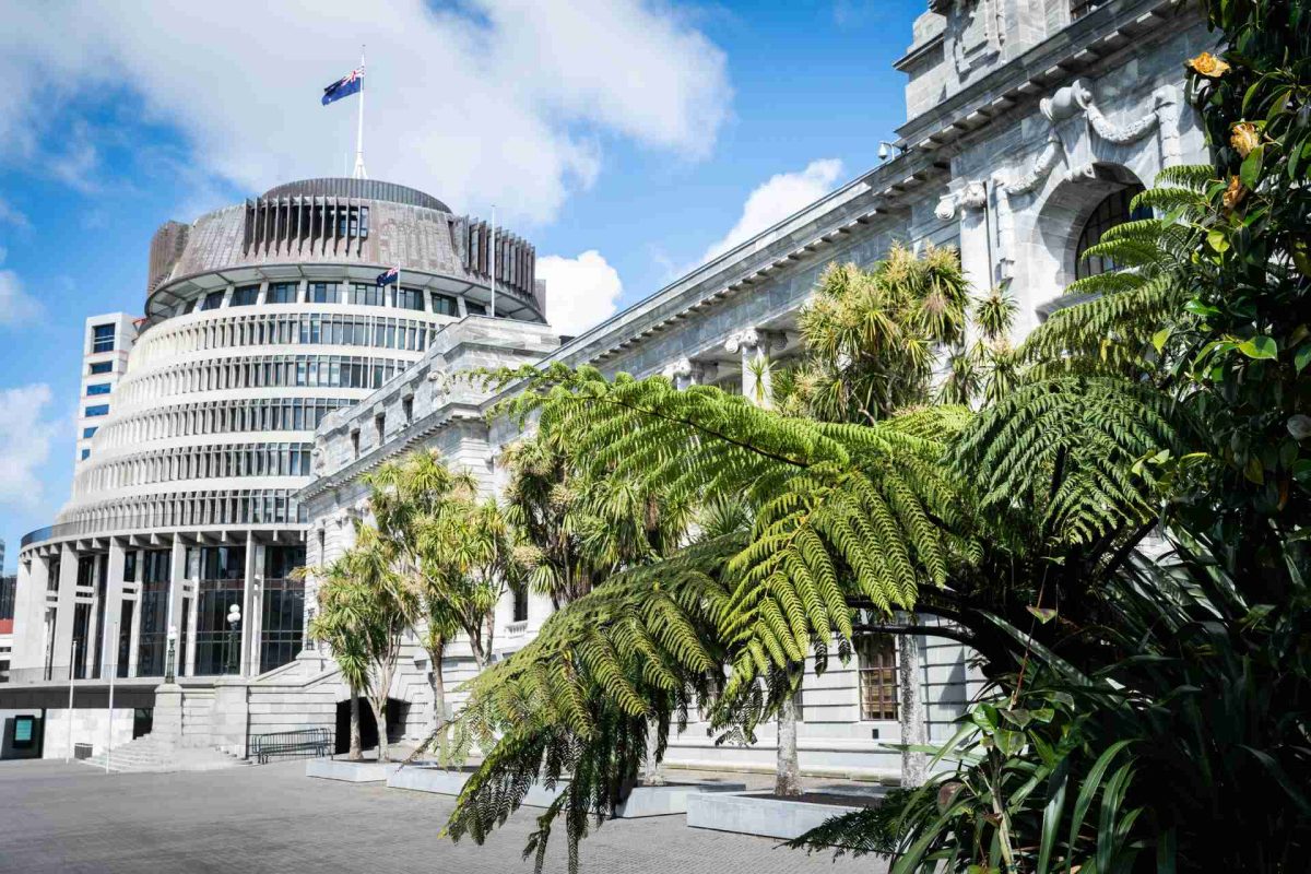 The Beehive and Parliament buildings in Wellington, New Zealand, with green trees and ferns in the foreground
