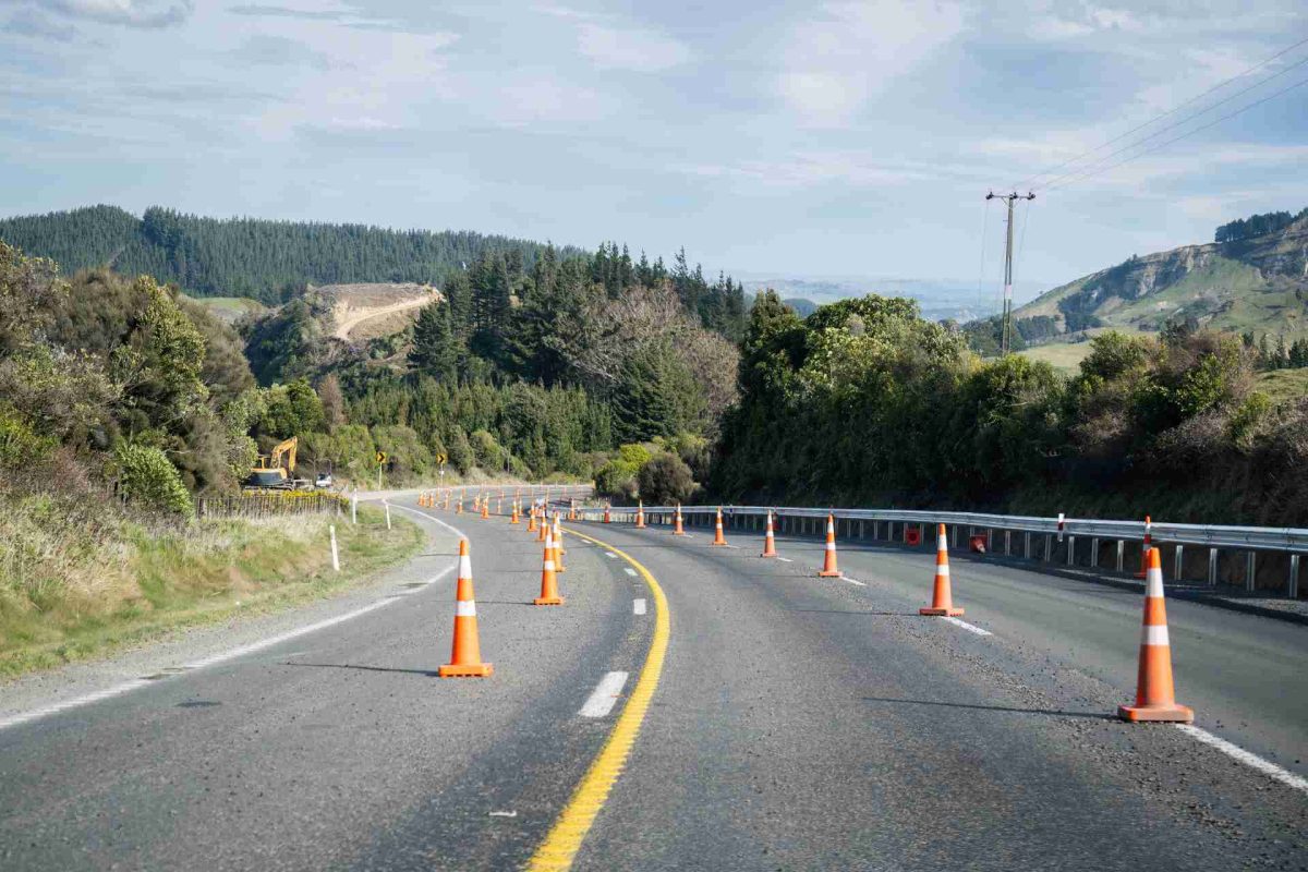 Road with traffic cones marking a construction zone, surrounded by trees and hills