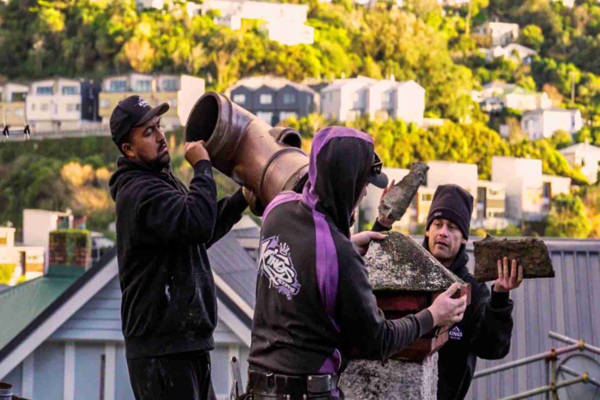 Three workers dismantling an old brick chimney on a rooftop