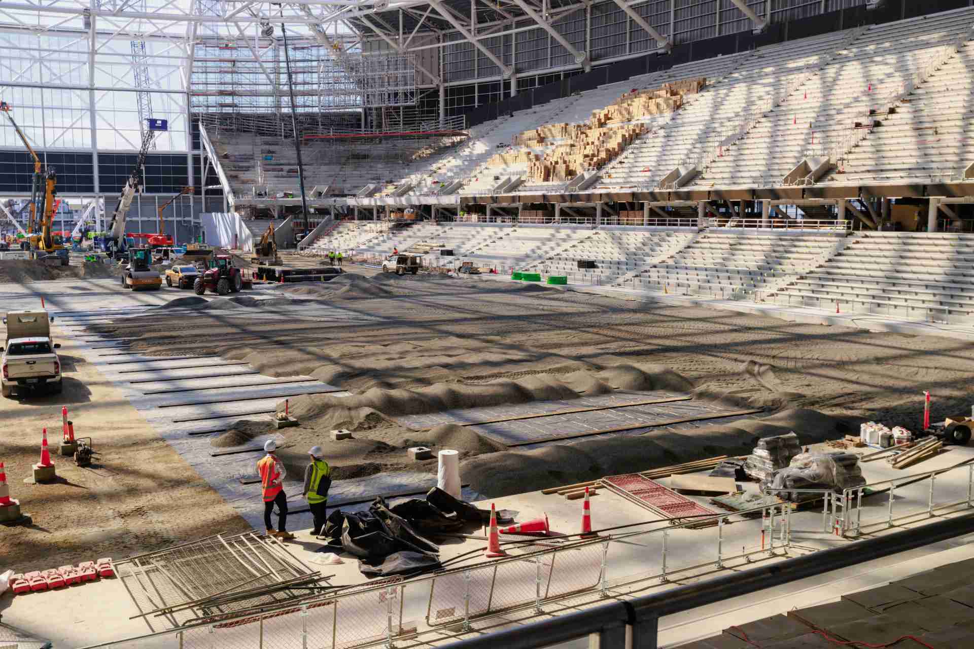 Stadium interior with seating tiers and construction work on the field area, workers and equipment visible